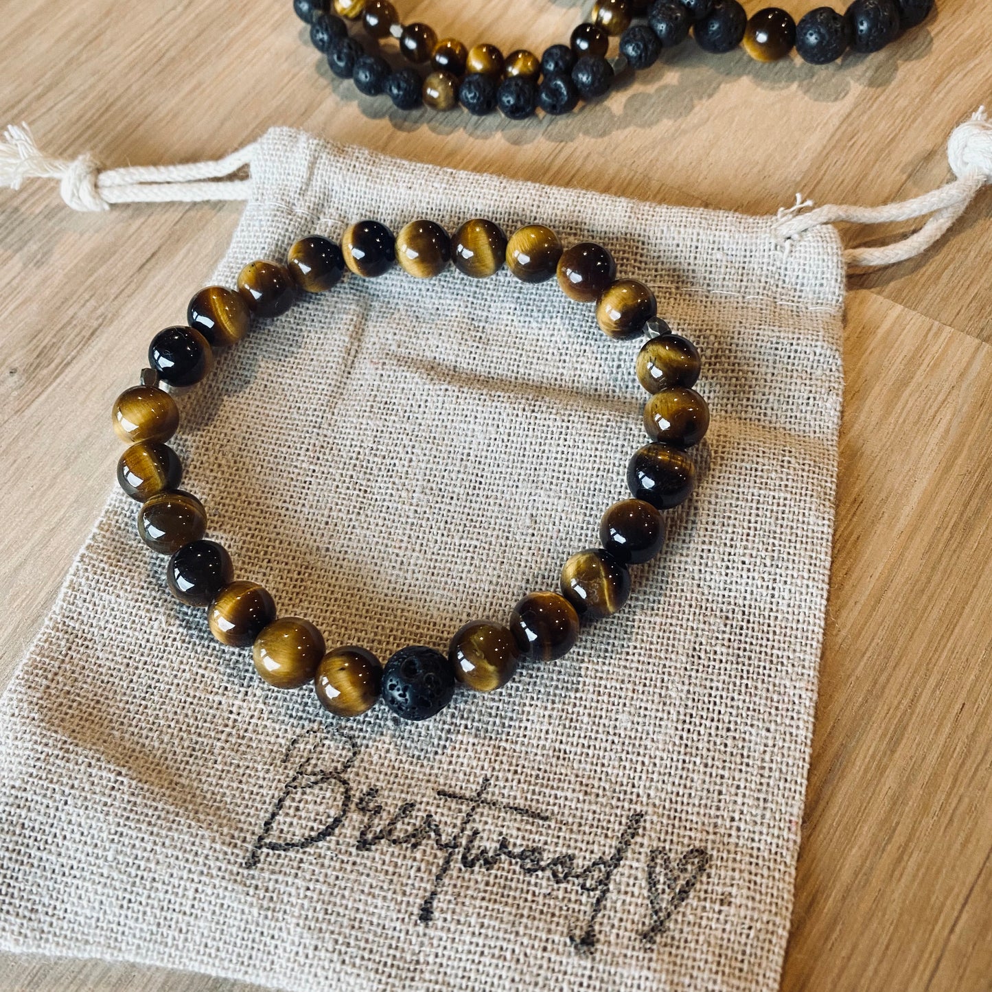 Tiger Eye 6 Aroma Bracelet - 6mm beaded diffuser bracelet made from natural tiger eye gemstone & a single black lava stone bead with antiqued gold faceted embellishments. Laid on cloth pouch/drawstring bag stamped with “Brentwood” and a heart.